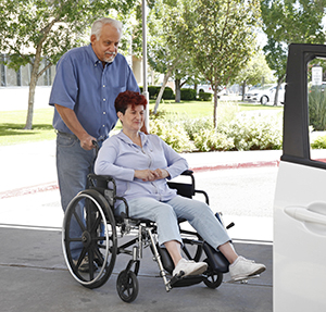 Man helping woman from wheelchair into car.